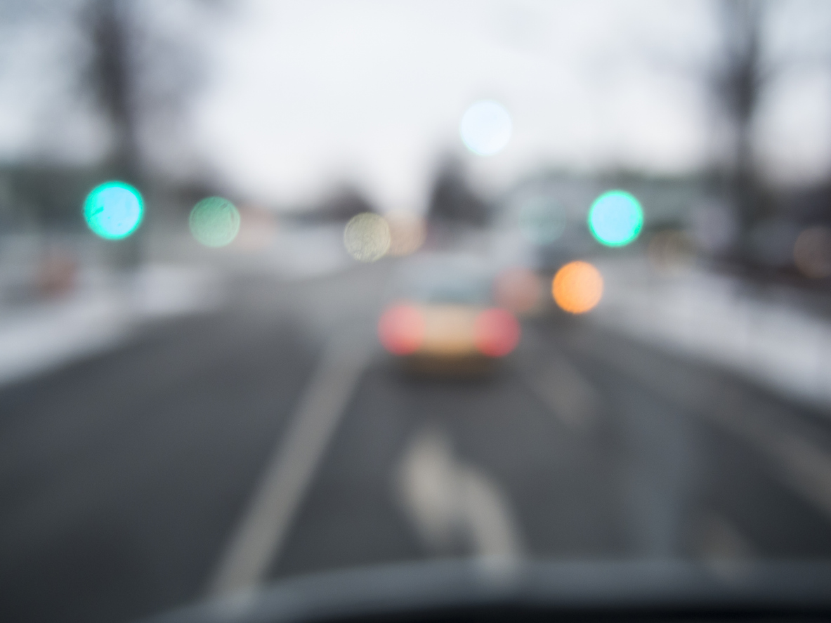 Strong impaired with a view through the windscreen of a vehicle on public road traffic at dawn.