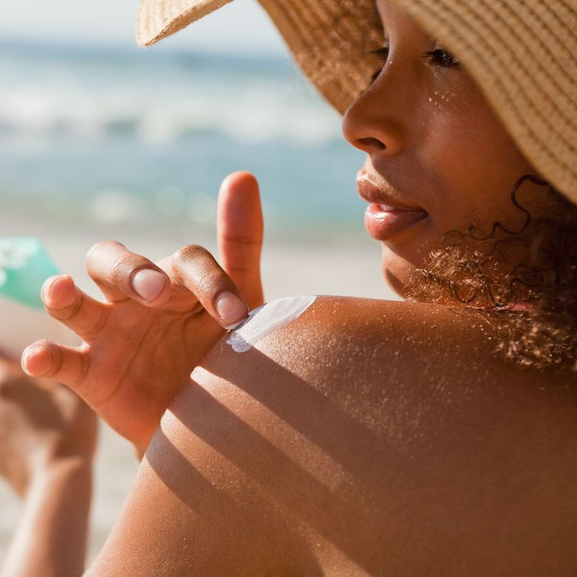 Young woman applying sunscreen on her shoulder while sitting on the beach