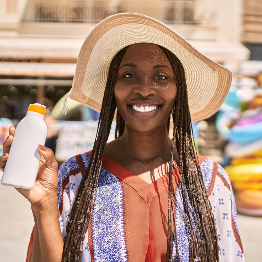Young african american woman smiling happy holding sunscreen lotion at the city.