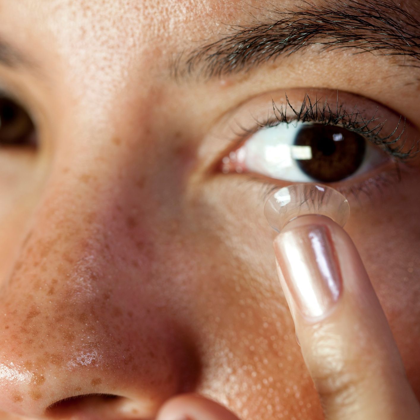 Eye contact from a pretty young mixed race woman inserting a contact lens into her eye. Macro focus on the lens and eyelash.